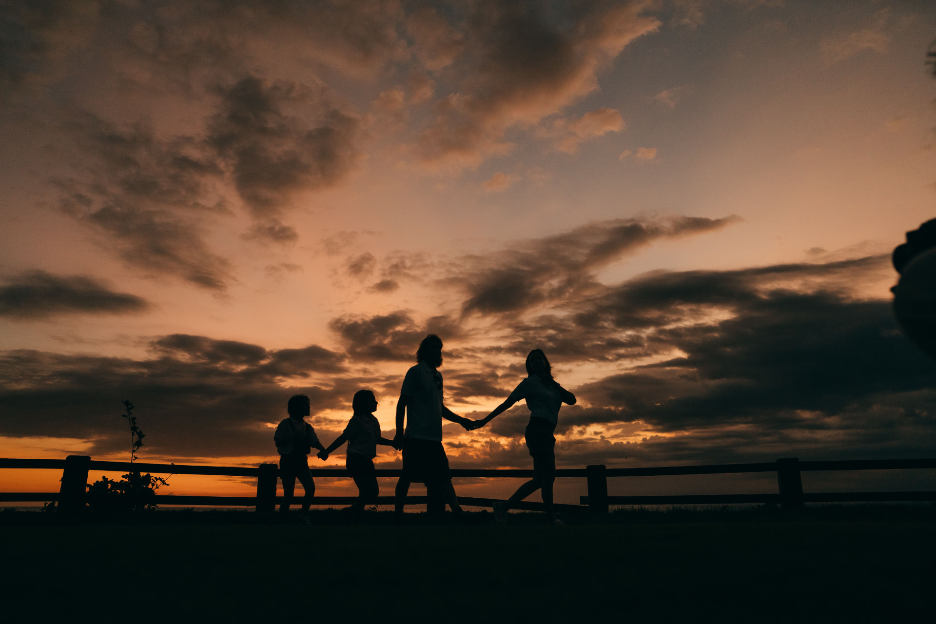 A family holding hands outdoors beneath a sunset sky